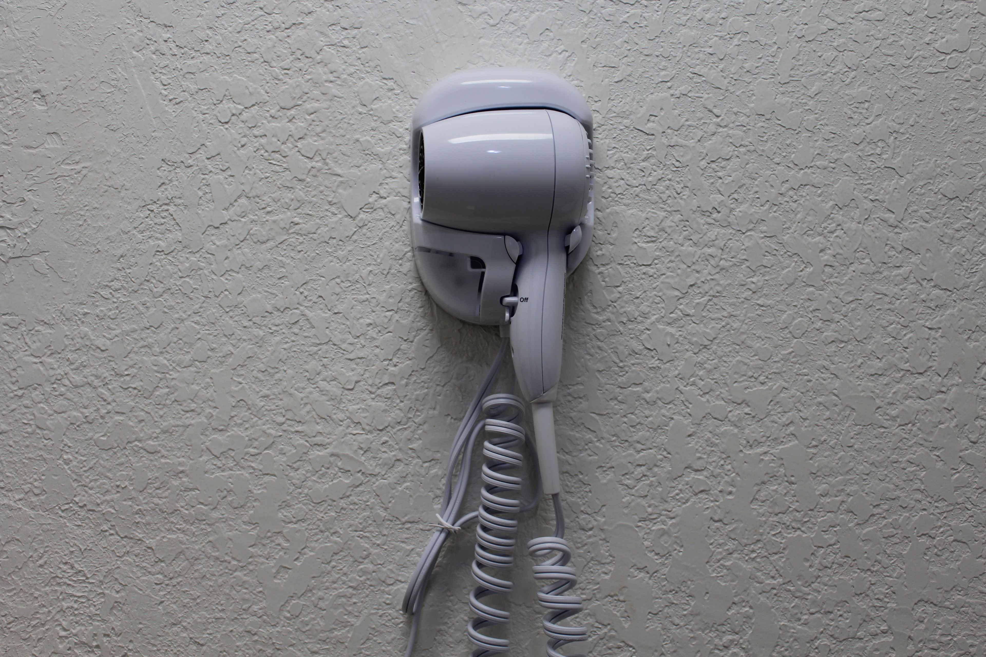 A hair dryer mounted on a textured wall.