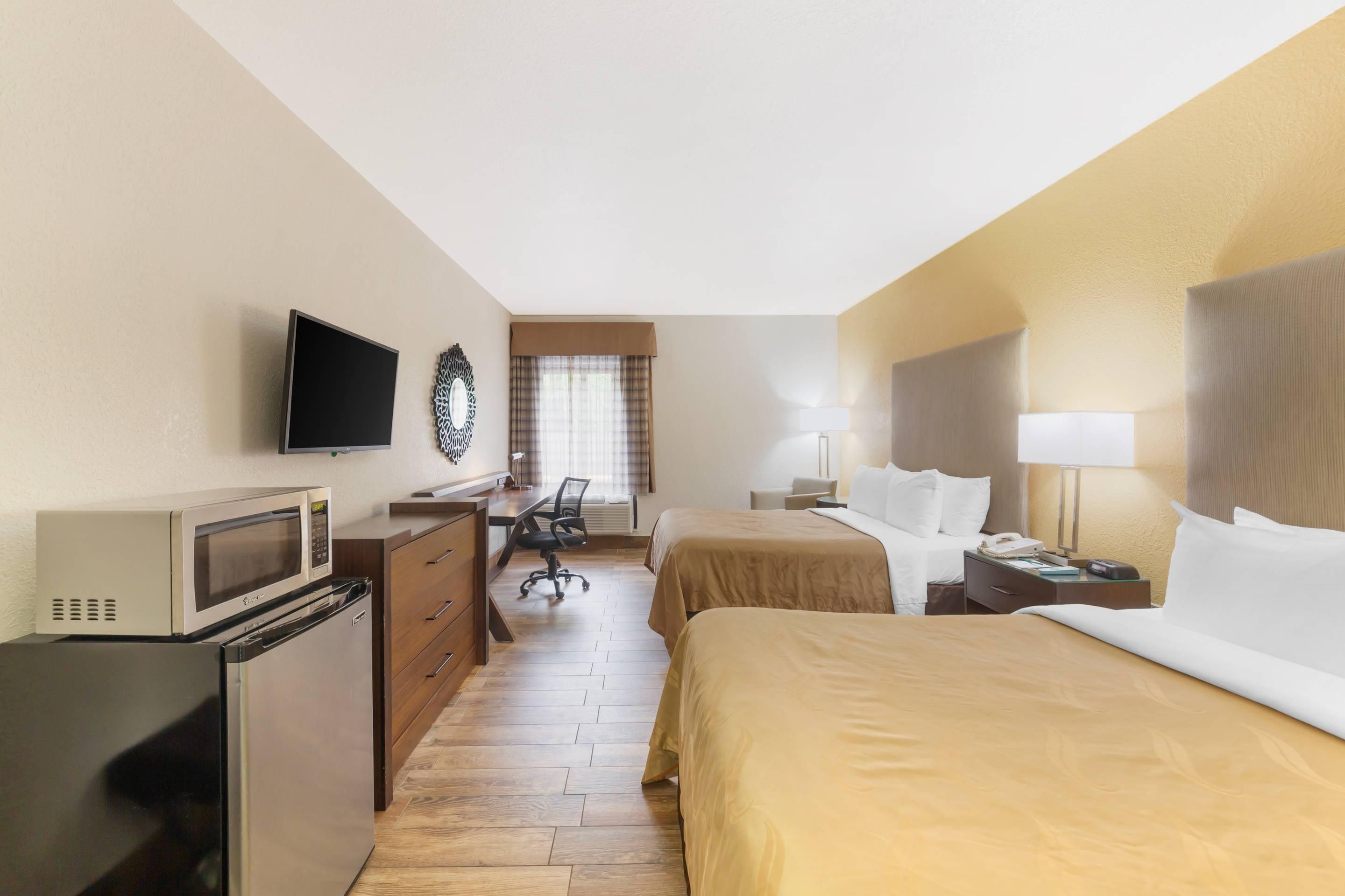 A hotel room with a bed, bedside table, lamp, desk with chair, and a television mounted on the wall.