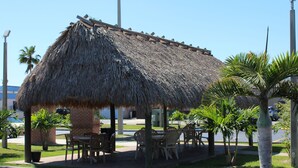 A thatched-roof outdoor seating area with tables and chairs, surrounded by palm trees and a brick building. - Quality Inn Florida City - Gateway to the Keys (Florida City)