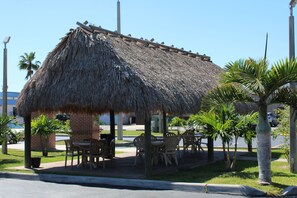 A thatched-roof outdoor seating area with tables and chairs, surrounded by palm trees and a brick building. - Quality Inn Florida City - Gateway to the Keys (Florida City)