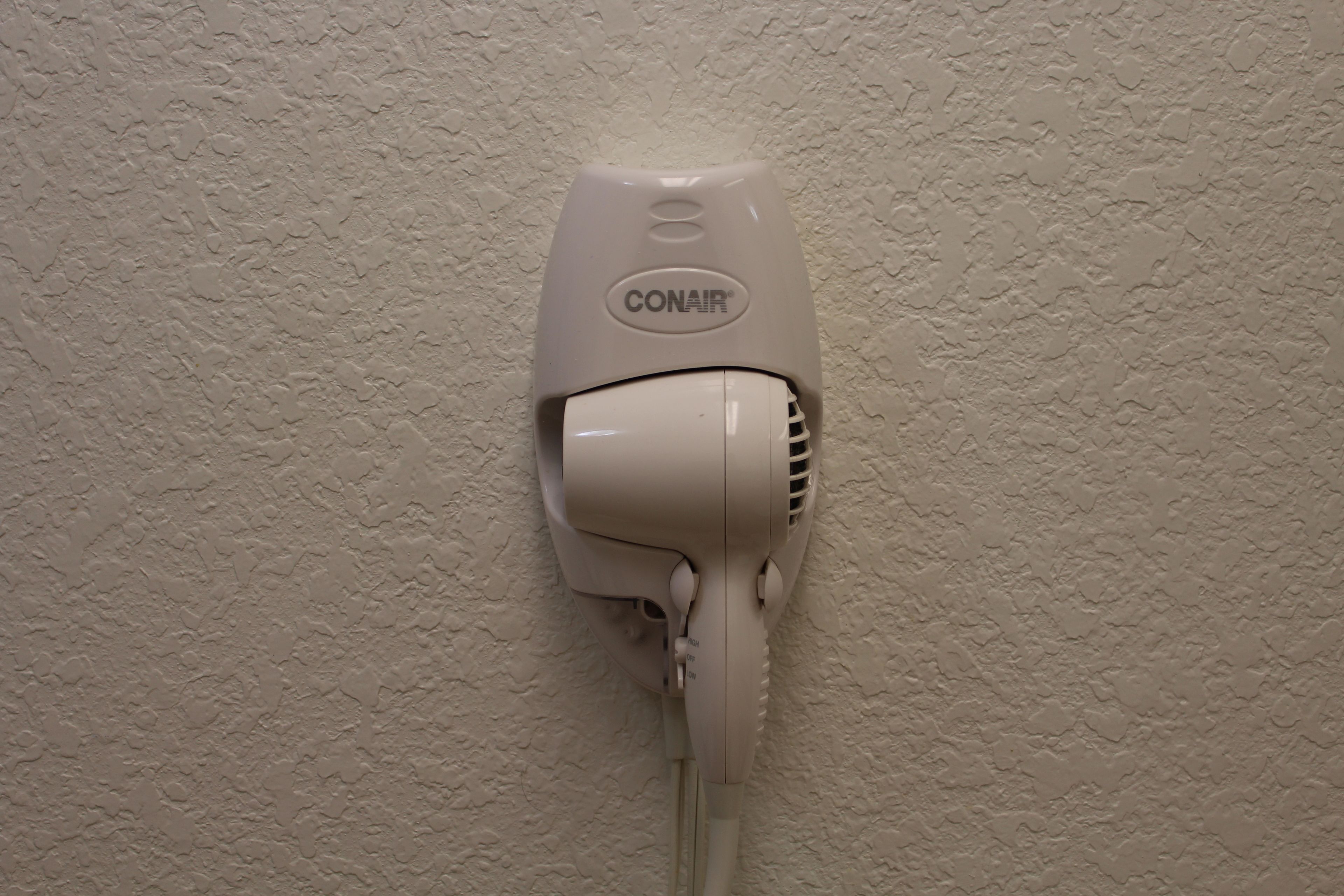 Un sèche-cheveux Conair blanc fixé sur un mur à texture.