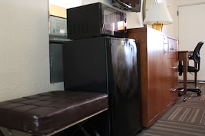 A compact room with a wooden desk, a chair, a bench, and a refrigerator. - Quality Inn Florida City - Gateway to the Keys (Florida City)
