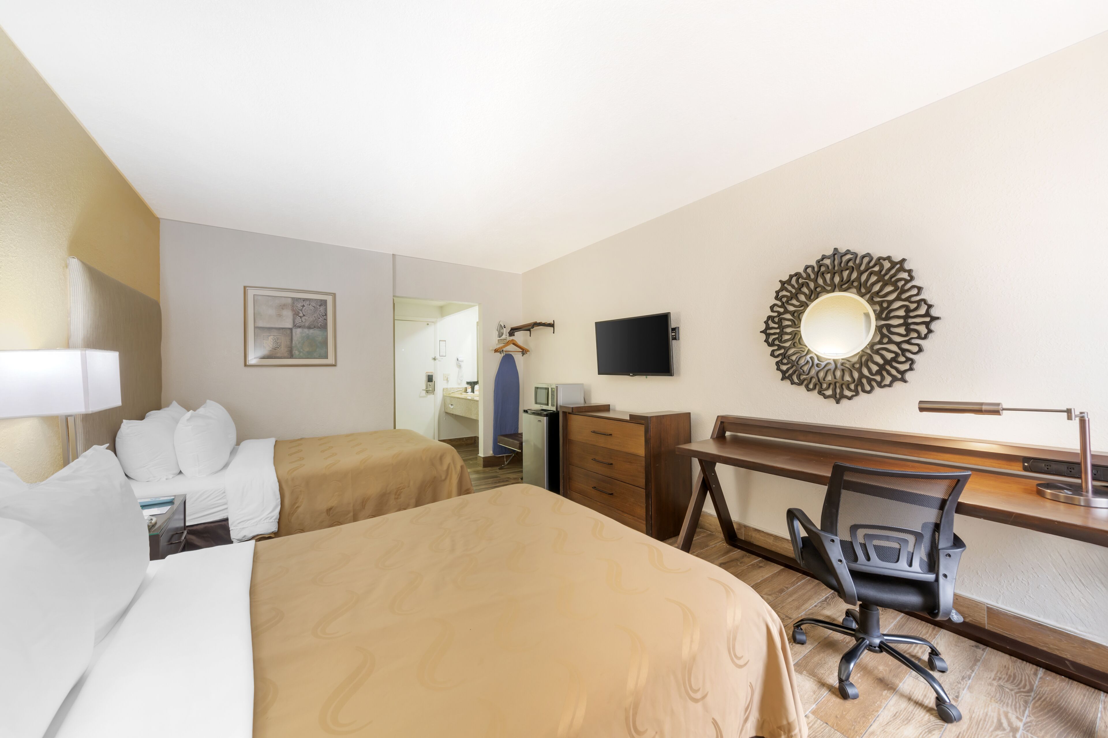 Une chambre d’hôtel avec deux lits, un bureau, une chaise, une télévision et un miroir au mur.
