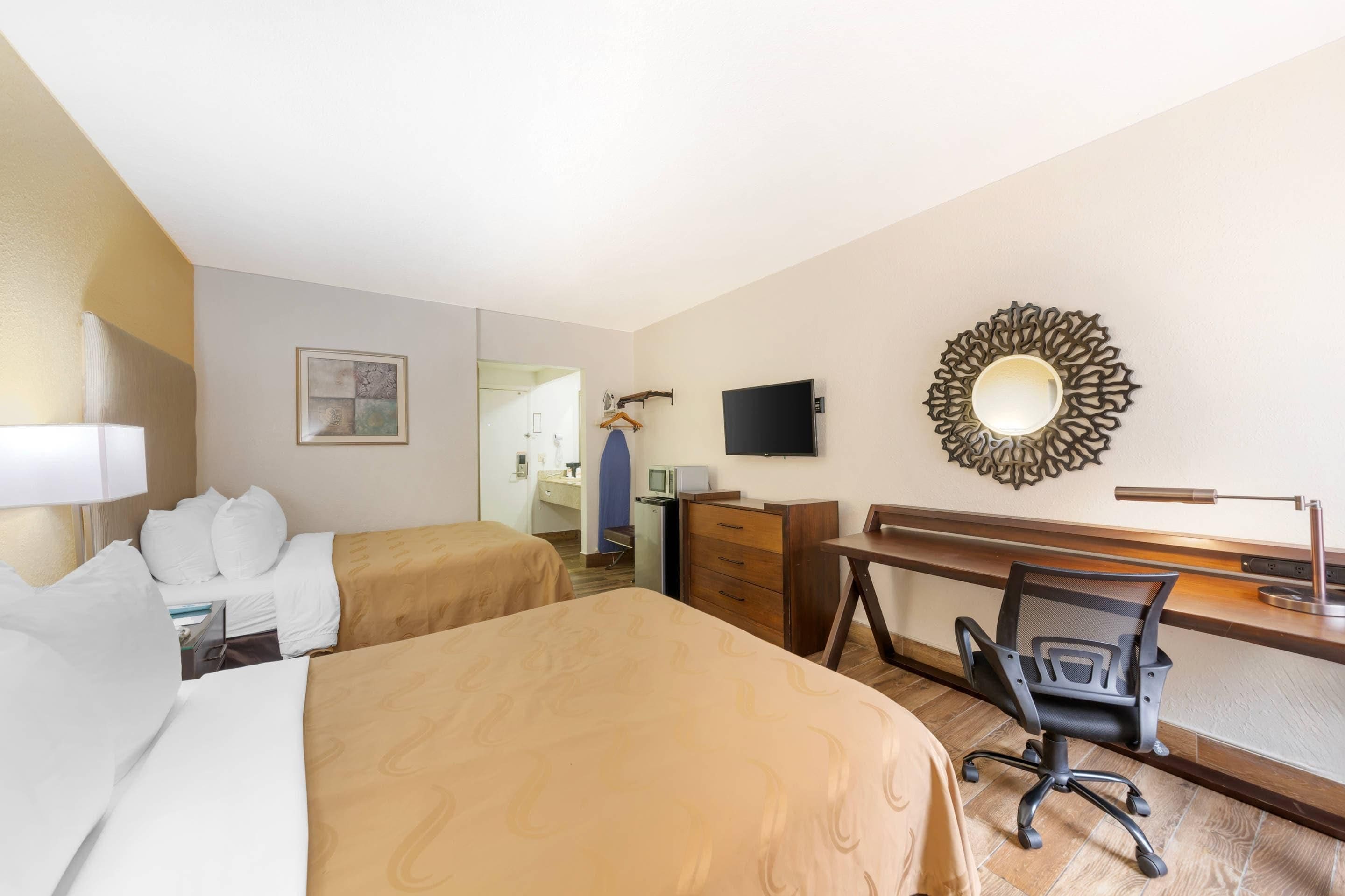 Une chambre d’hôtel avec deux lits, un bureau, une chaise, une télévision et un miroir décoratif.