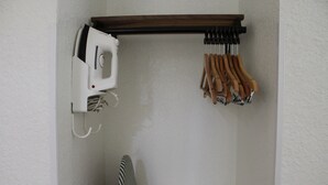 A corner of a room with a white wall, a wooden shelf holding a white appliance and a set of wooden-handled tools, and a striped chair. - Quality Inn Florida City - Gateway to the Keys (Florida City)