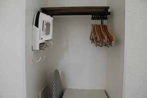 A corner of a room with a white wall, a wooden shelf holding a white appliance and a set of wooden-handled tools, and a striped chair. - Quality Inn Florida City - Gateway to the Keys (Florida City)