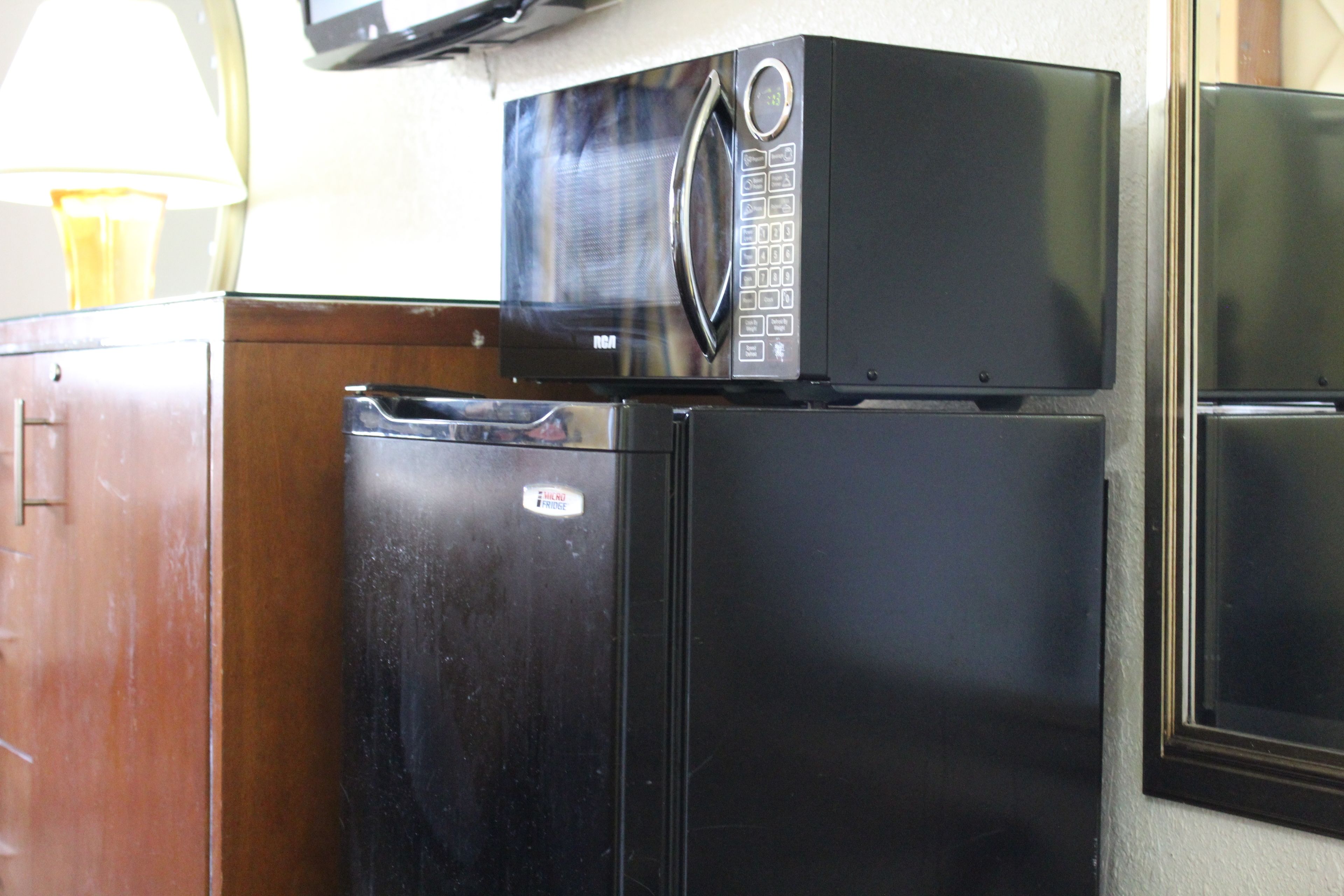 A black refrigerator with a microwave on top, a wooden cabinet to the left, and a window to the right.