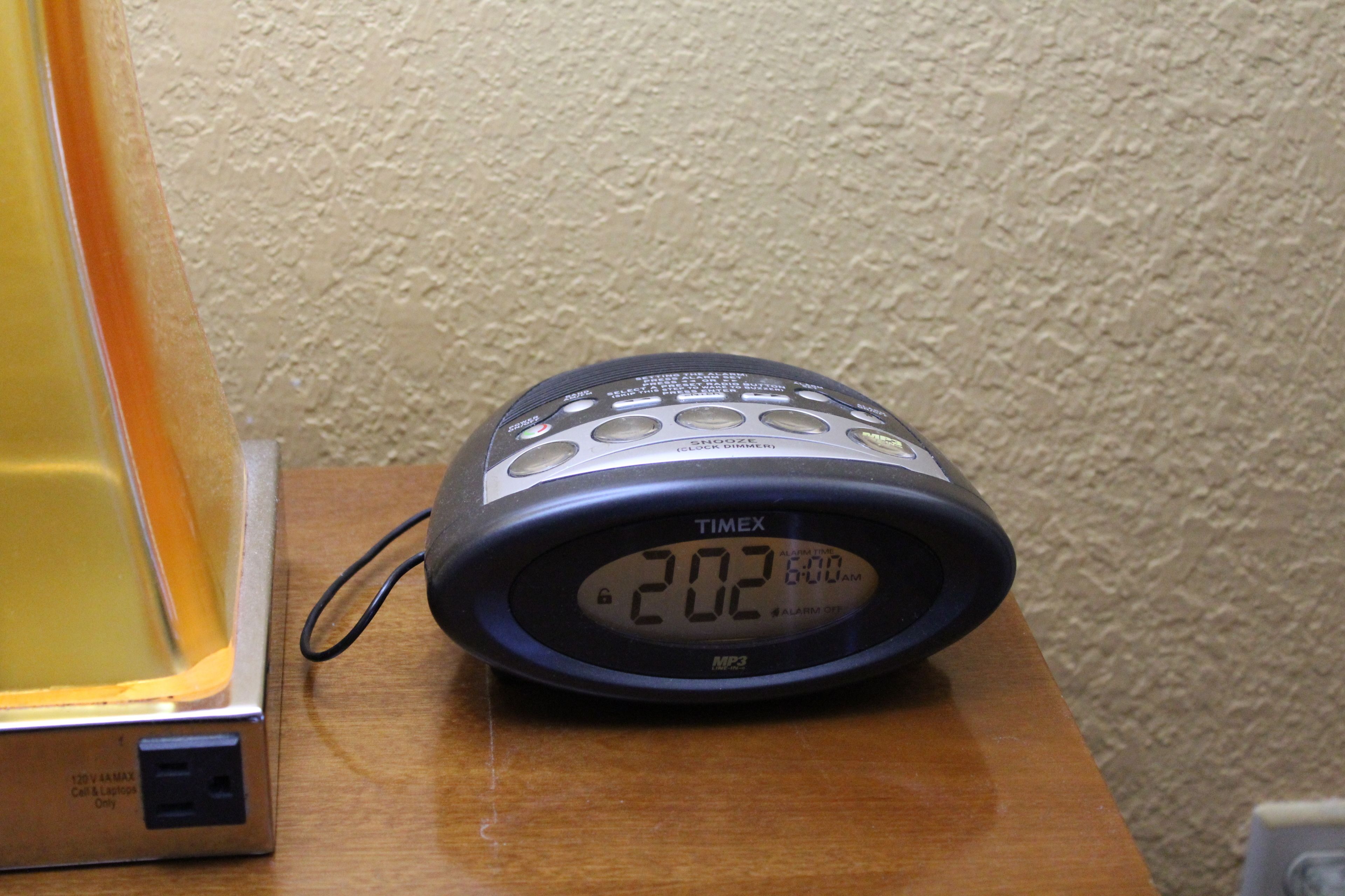 A TIMEX alarm clock on a wooden surface with a textured wall in the background.