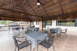 An outdoor patio area with tables and chairs, a thatched roof, and a view of the street.