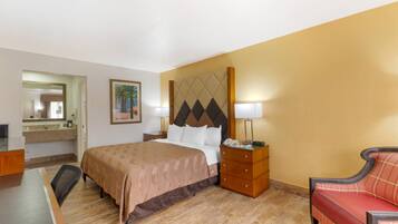 A hotel room with a bed, bedside table, lamp, chair, and a mirror.