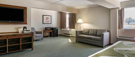 A hotel room with a large bed, a sofa, a desk with a computer, a television, and a window with curtains.
