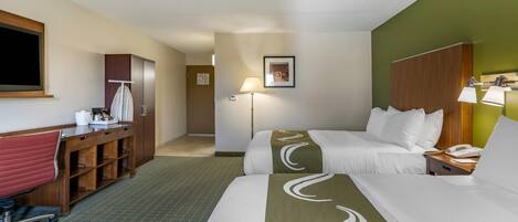 A hotel room with a bed, desk, chair, and a lamp.