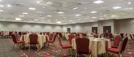 Un salón de conferencias amplio con filas de mesas y sillas, piso alfombrado e iluminación en el techo.