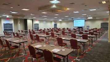 Une salle de conférence avec des rangées de tables et de chaises, un écran de projection et un sol recouvert de moquette.