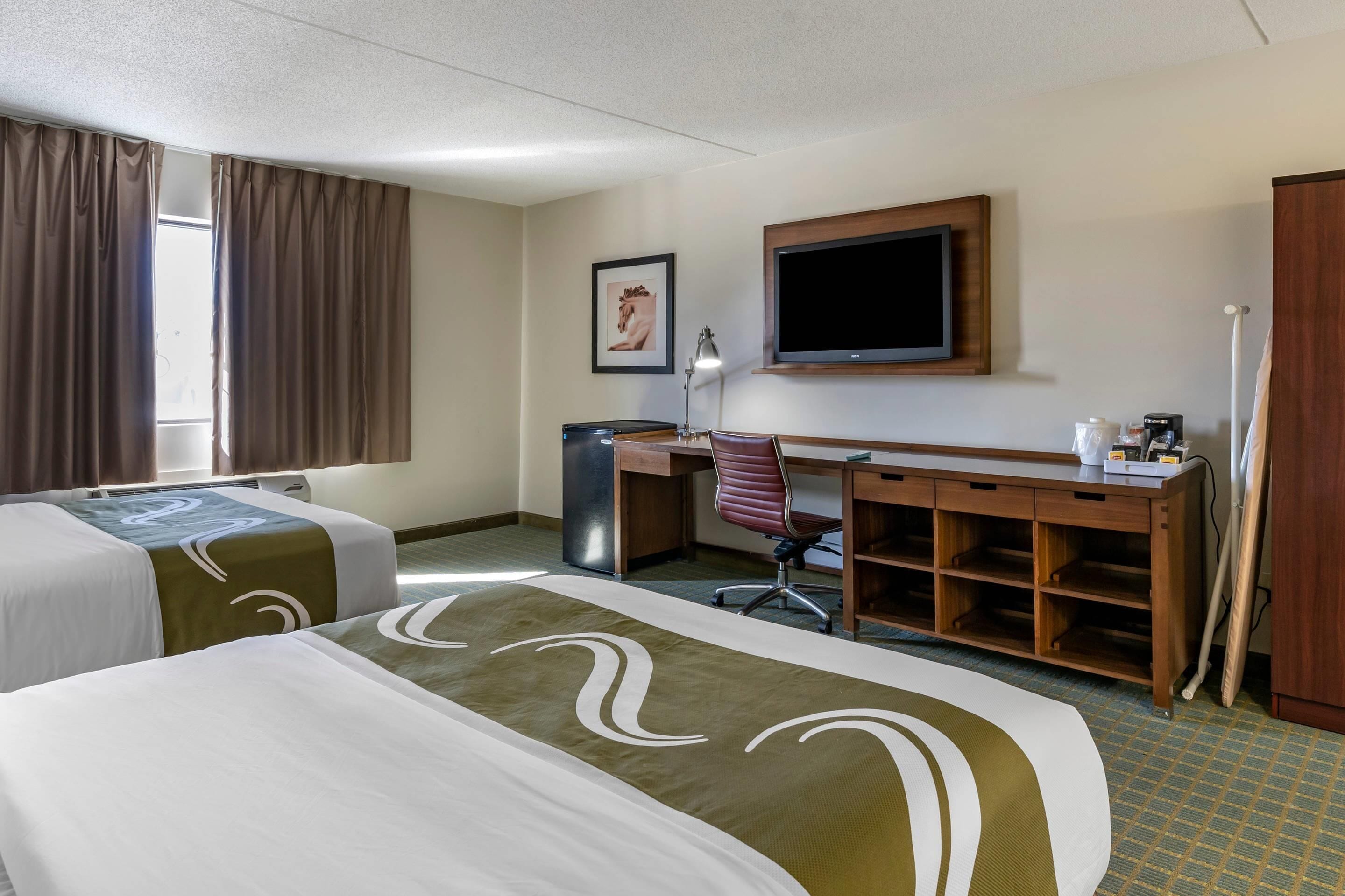 A hotel room with two beds, a desk, a chair, a television, and a wardrobe.