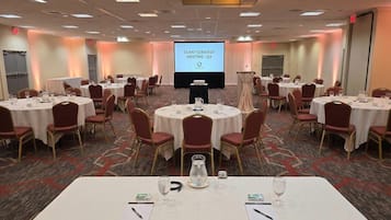 Uma sala de conferências com mesas redondas, cadeiras e um ecrã de apresentação.