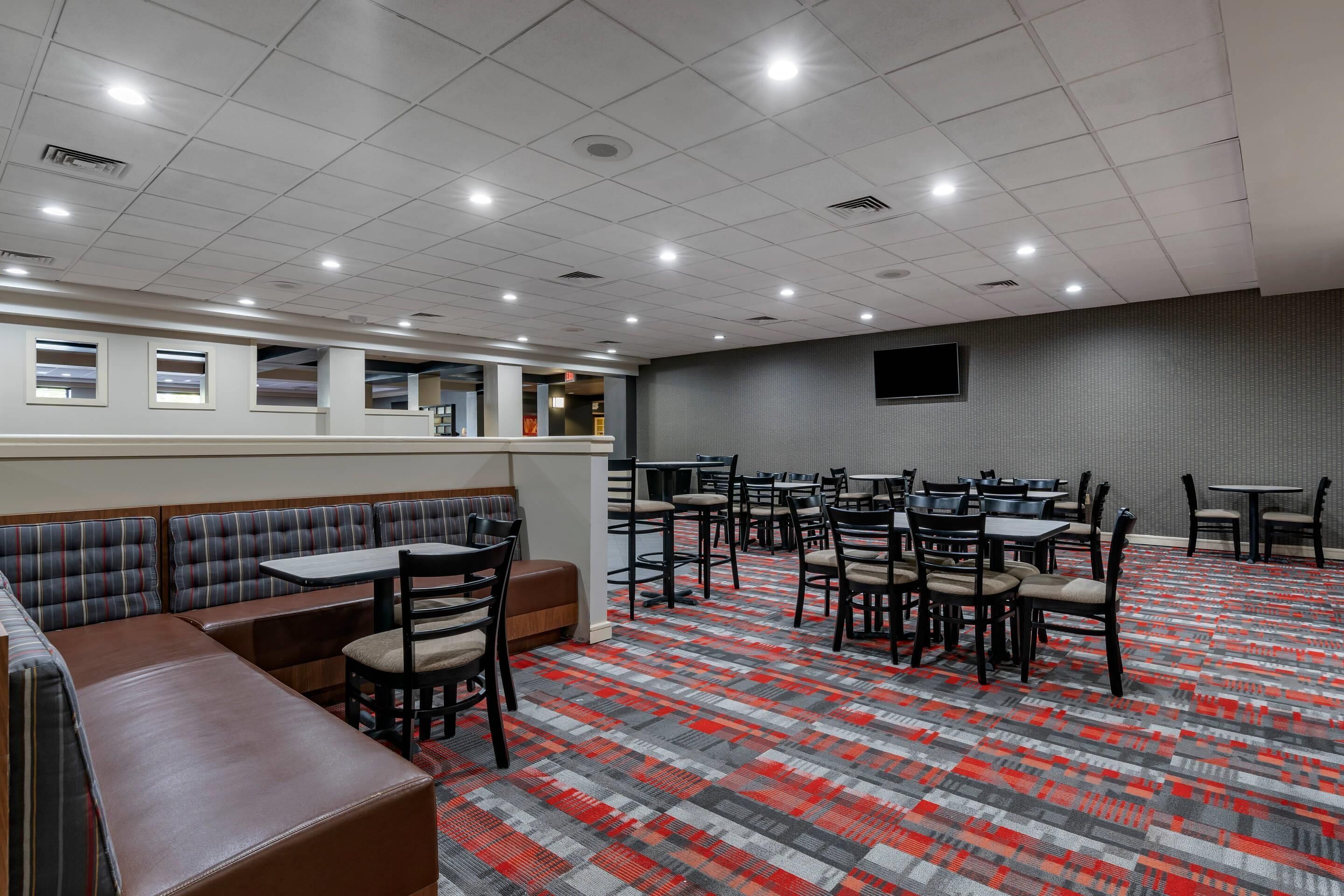A spacious dining area with booths and tables, a patterned carpet, and a flat-screen TV mounted on the wall.