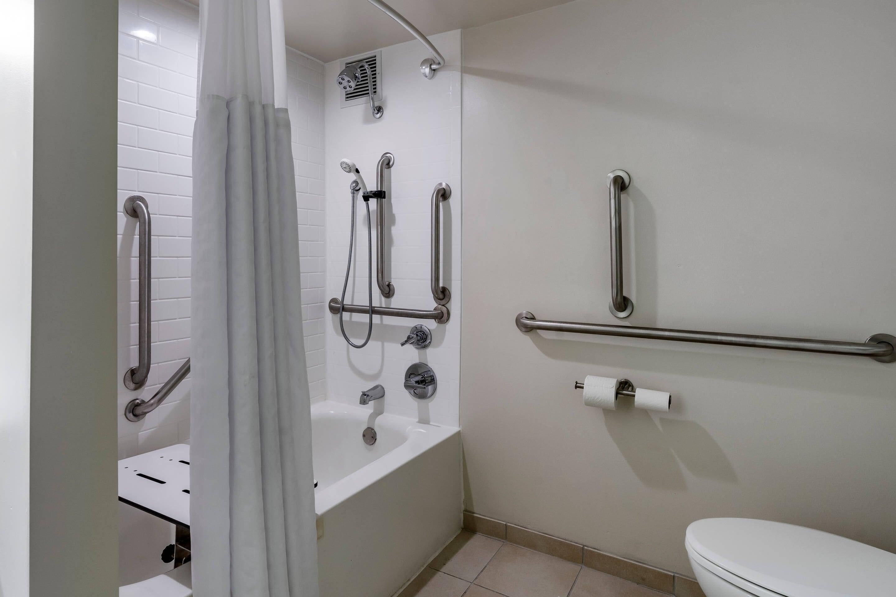 A bathroom with a bathtub, toilet, shower, and handrails.