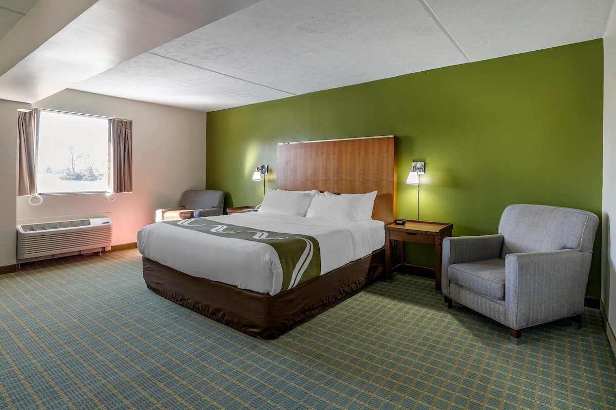 A hotel room with a bed, a chair, a nightstand, and a window with curtains.