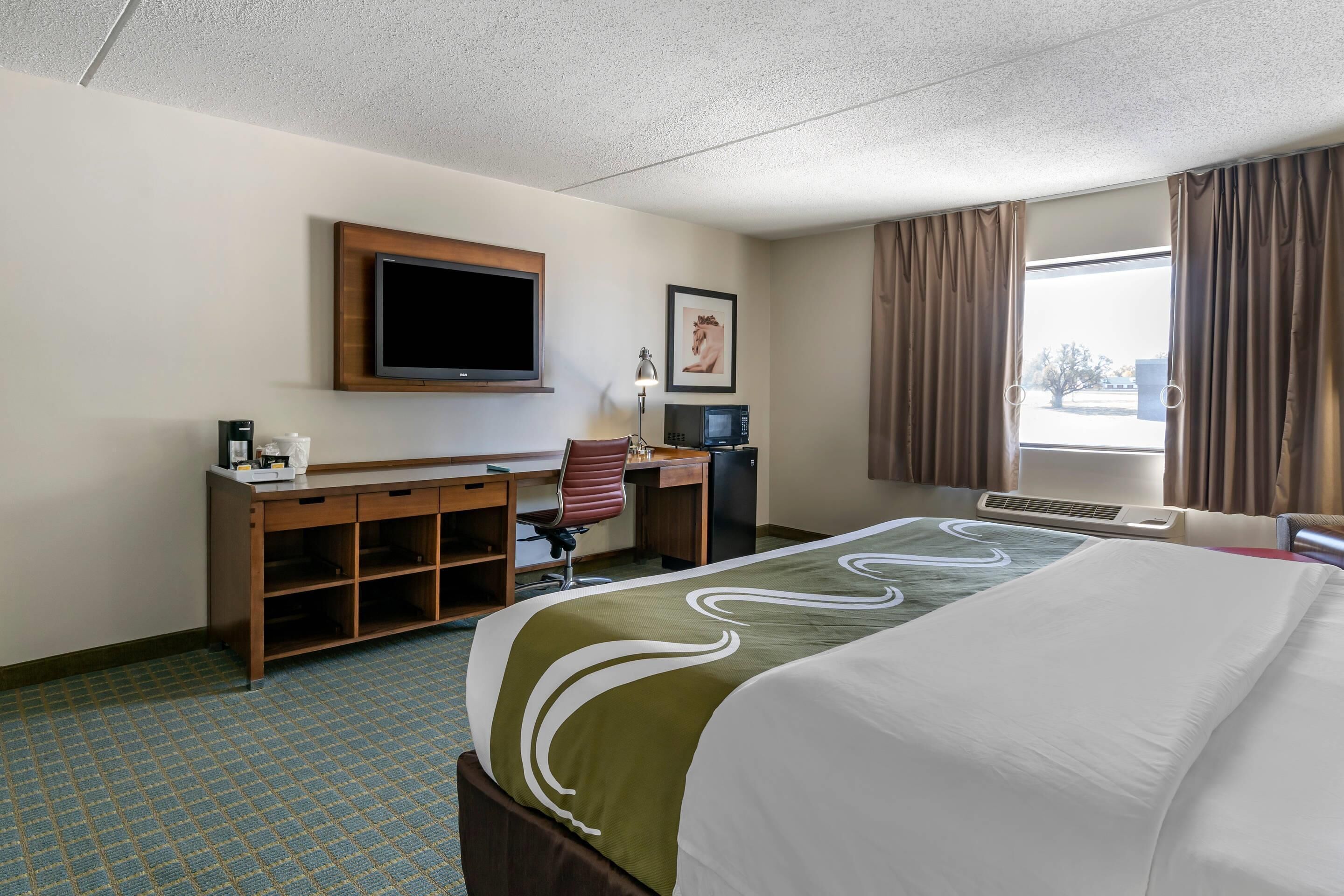 Habitación de hotel con cama, escritorio con computadora, televisión y ventana con cortinas.