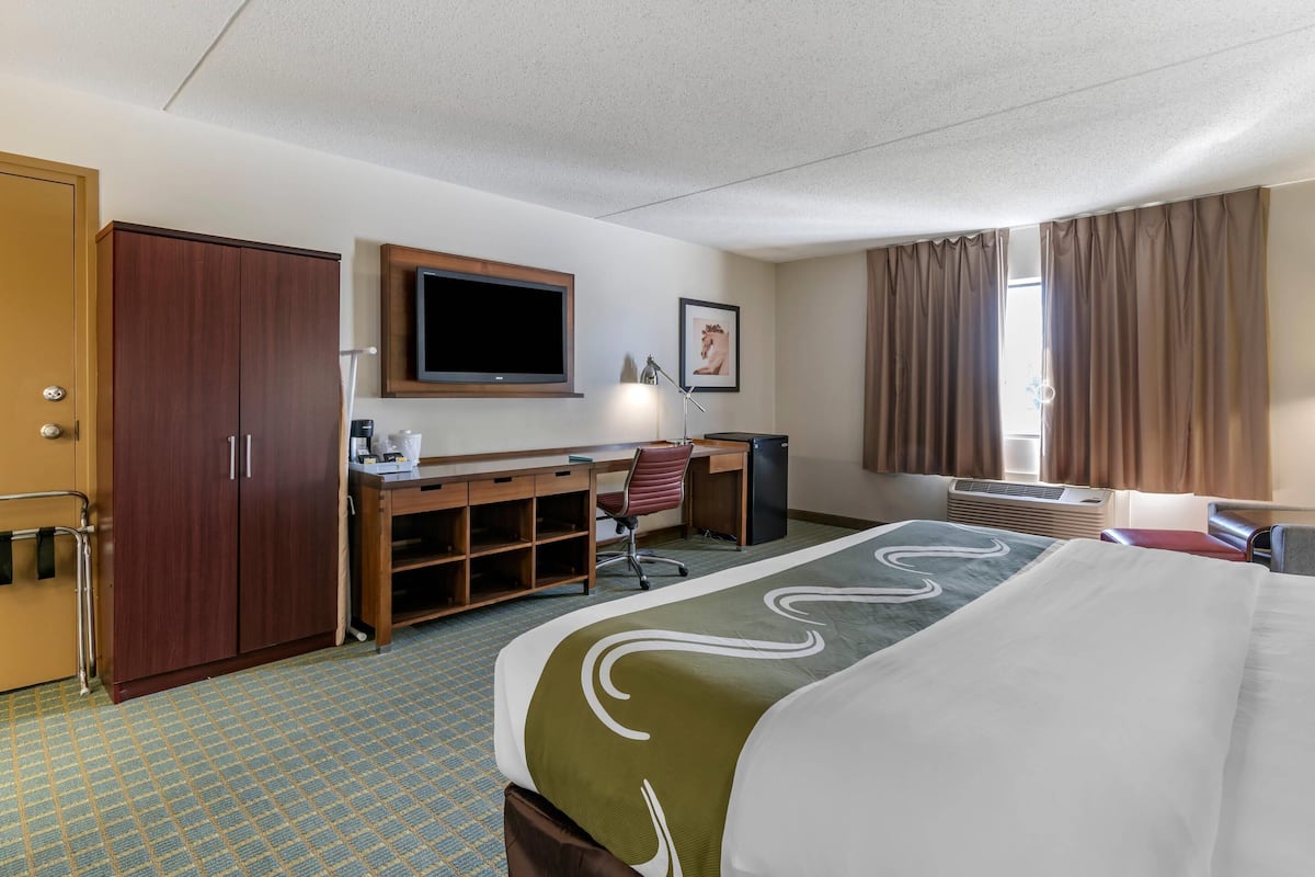 A hotel room with a bed, desk, chair, television, wardrobe, and air conditioning unit.