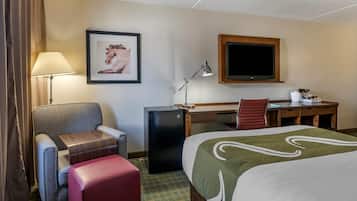 Een hotelkamer met een bed, een bureau, een stoel, een kleine koelkast, een lamp en een televisie.