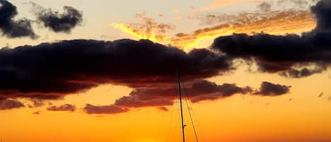 A sunset over a body of water with a sailboat and a dock in the foreground.