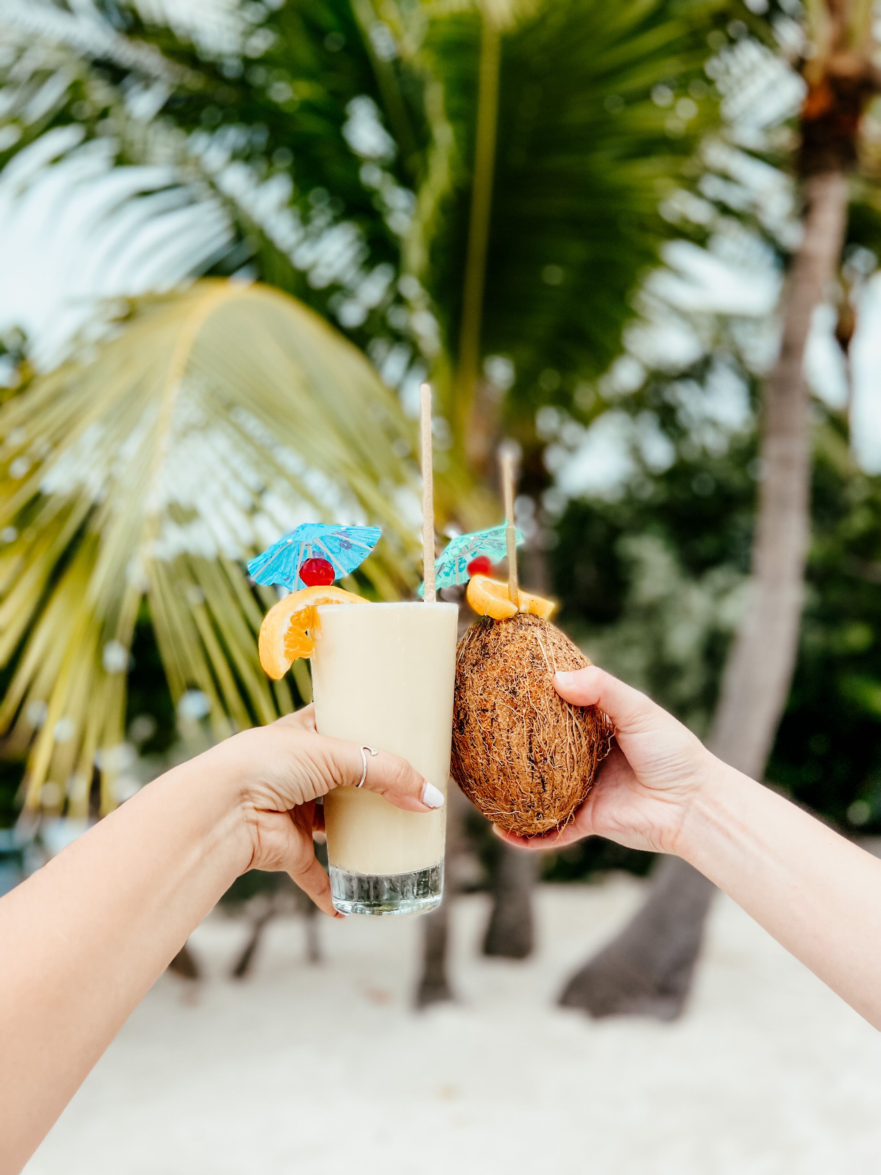 Two hands holding a drink and a coconut.