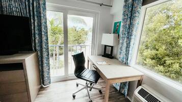 A room with a desk, chair, and large window with curtains.
