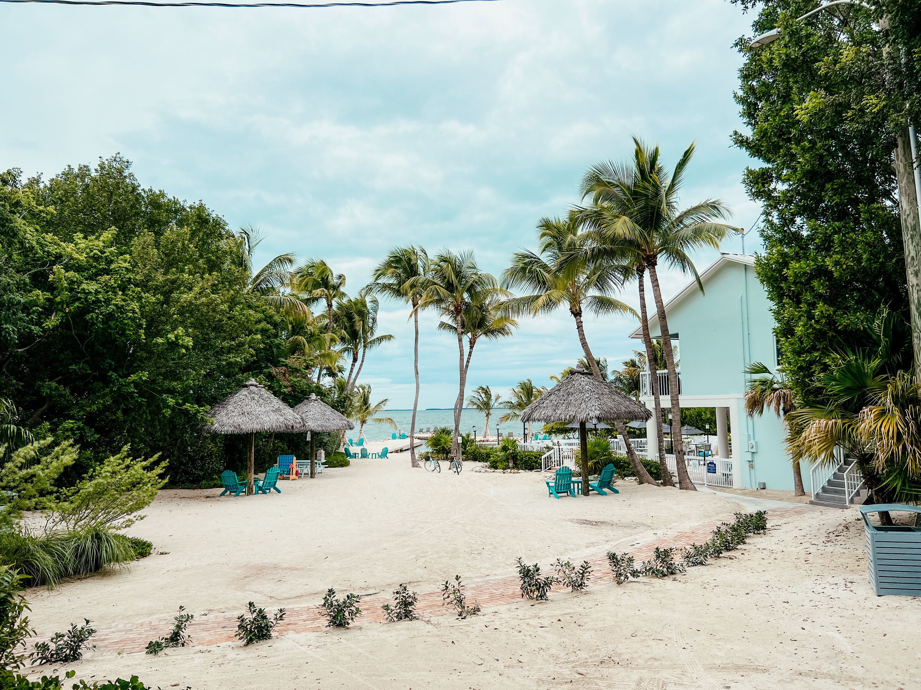 A beachside resort with thatched umbrellas, palm trees, and a light blue building.