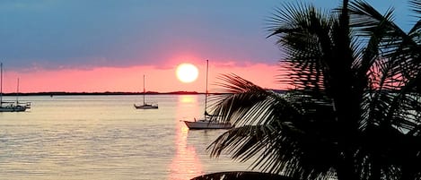 Un atardecer sobre aguas tranquilas con barcos y palmeras.