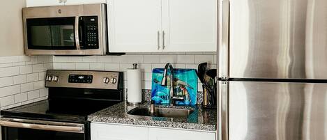 Ett modernt kök med vita skåp, vitvaror i rostfritt stål, en bänkskiva i granit och en blå dekorativ detalj vid diskbänken.