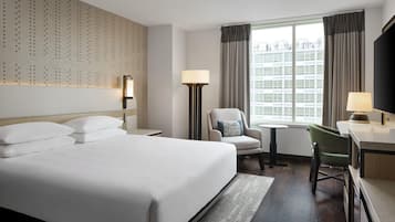 Habitación de hotel con una cama grande, un escritorio, una silla, una lámpara y vistas a un edificio a través de la ventana.