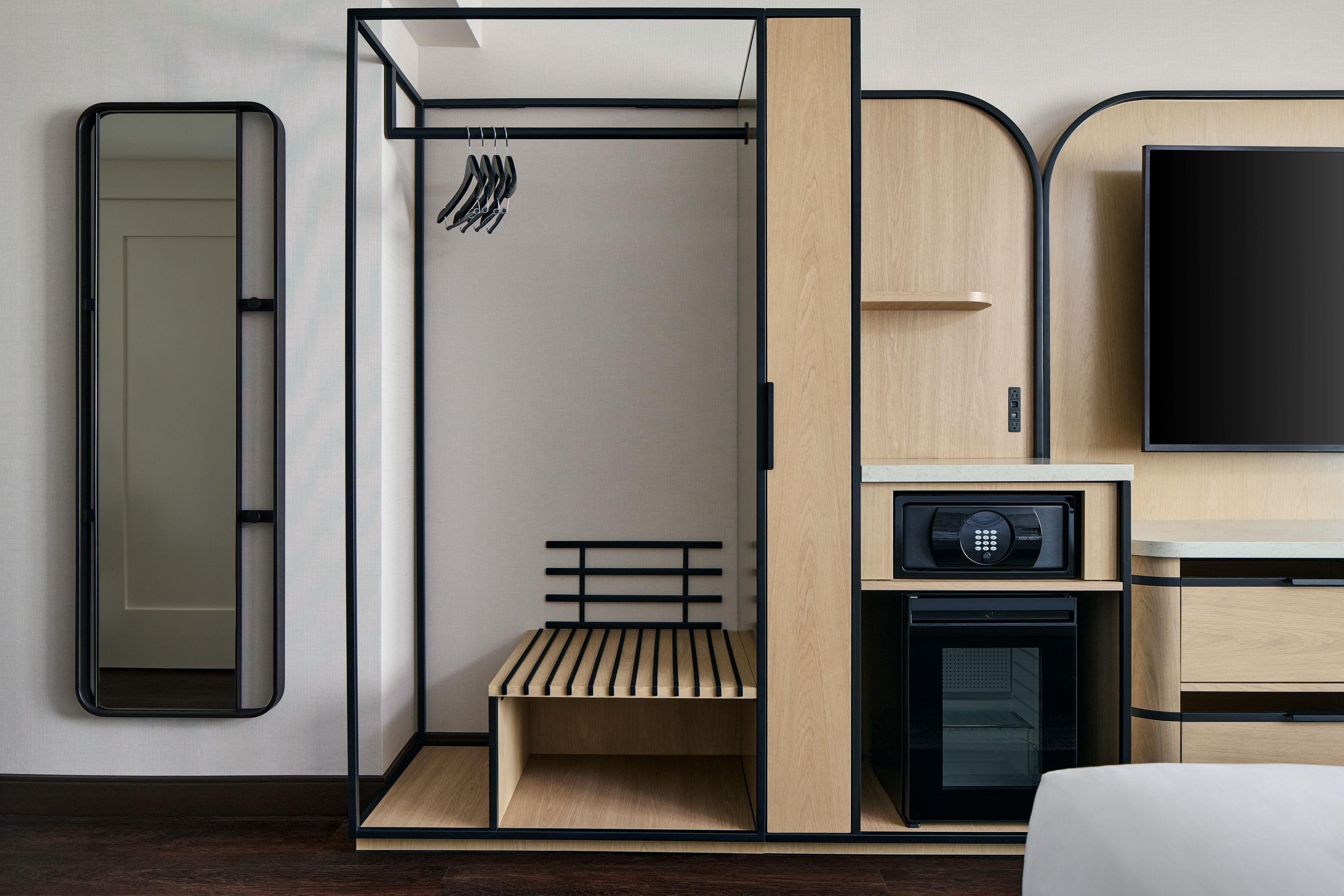 A modern hotel room with a bed, a built-in wardrobe, a seating area, a television, and a microwave.
