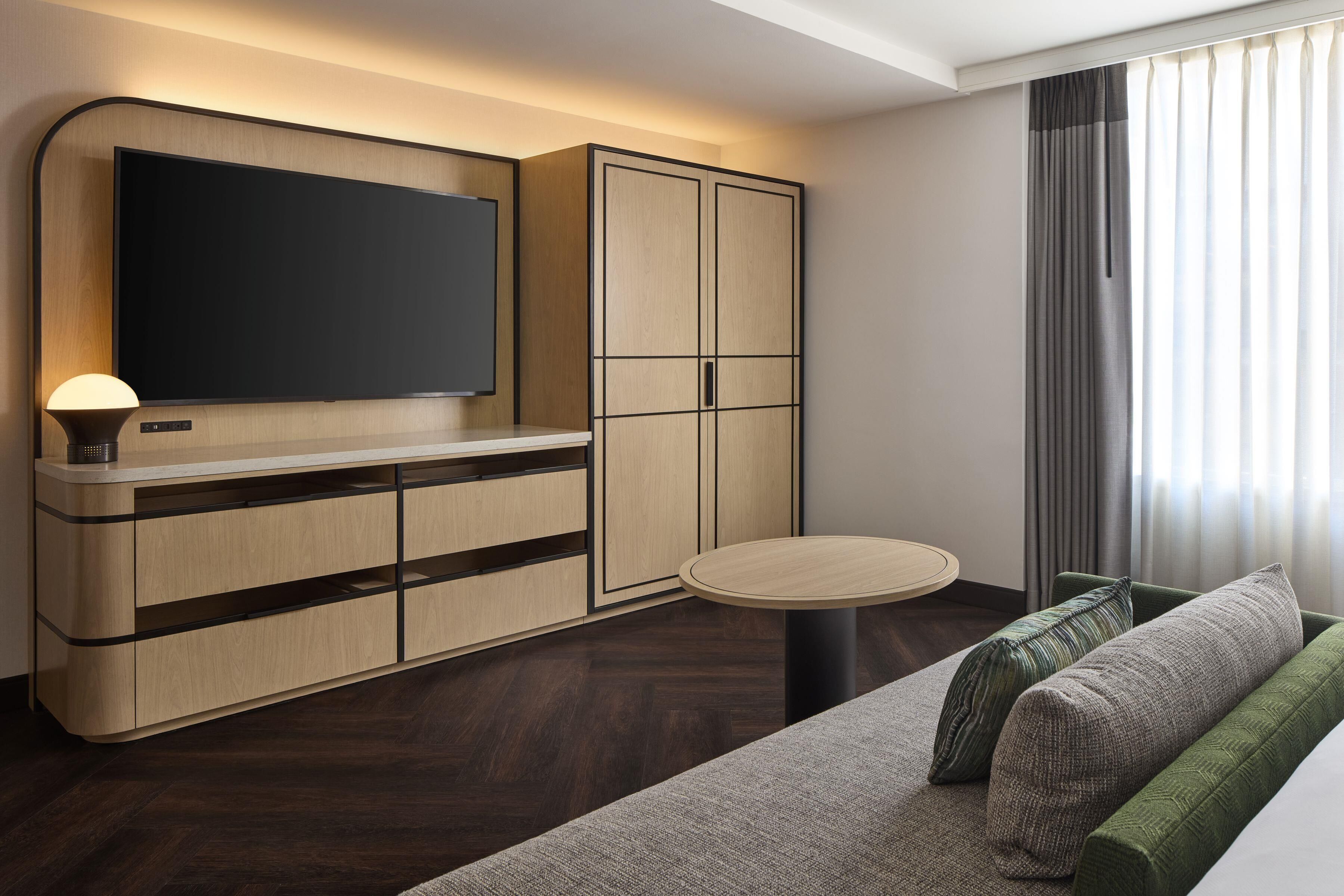 Une chambre moderne dotée d’une télévision à écran plat, de meubles en bois, d’une table ronde et d’un canapé avec des coussins.