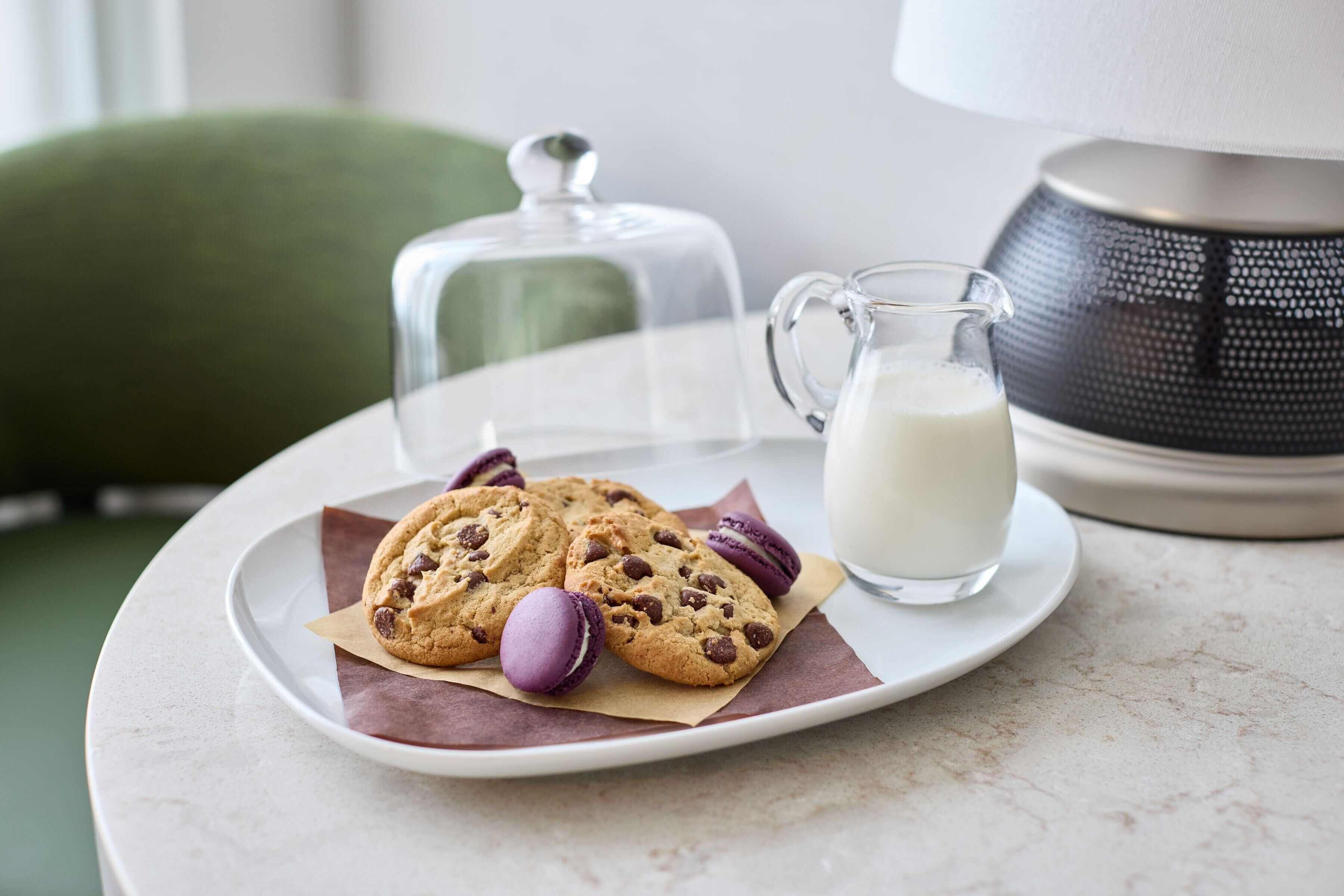 A plate with cookies and macarons, a milk jug, and a lamp on a table.