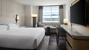 Habitación de hotel con una cama grande, un escritorio, una silla, un televisor y una ventana con cortinas.
