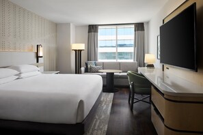 A hotel room with a large bed, a desk, a chair, a TV, and a window with curtains.