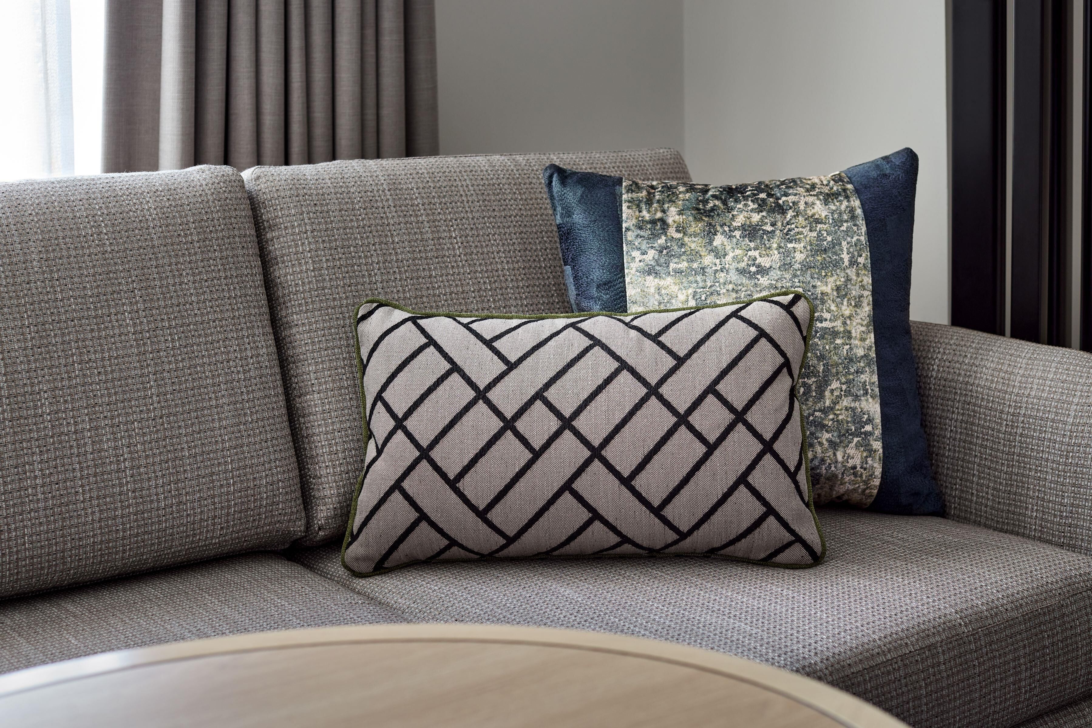 Un canapé avec trois coussins : un avec un motif géométrique, un autre avec un motif texturé et un troisième de couleur unie.
