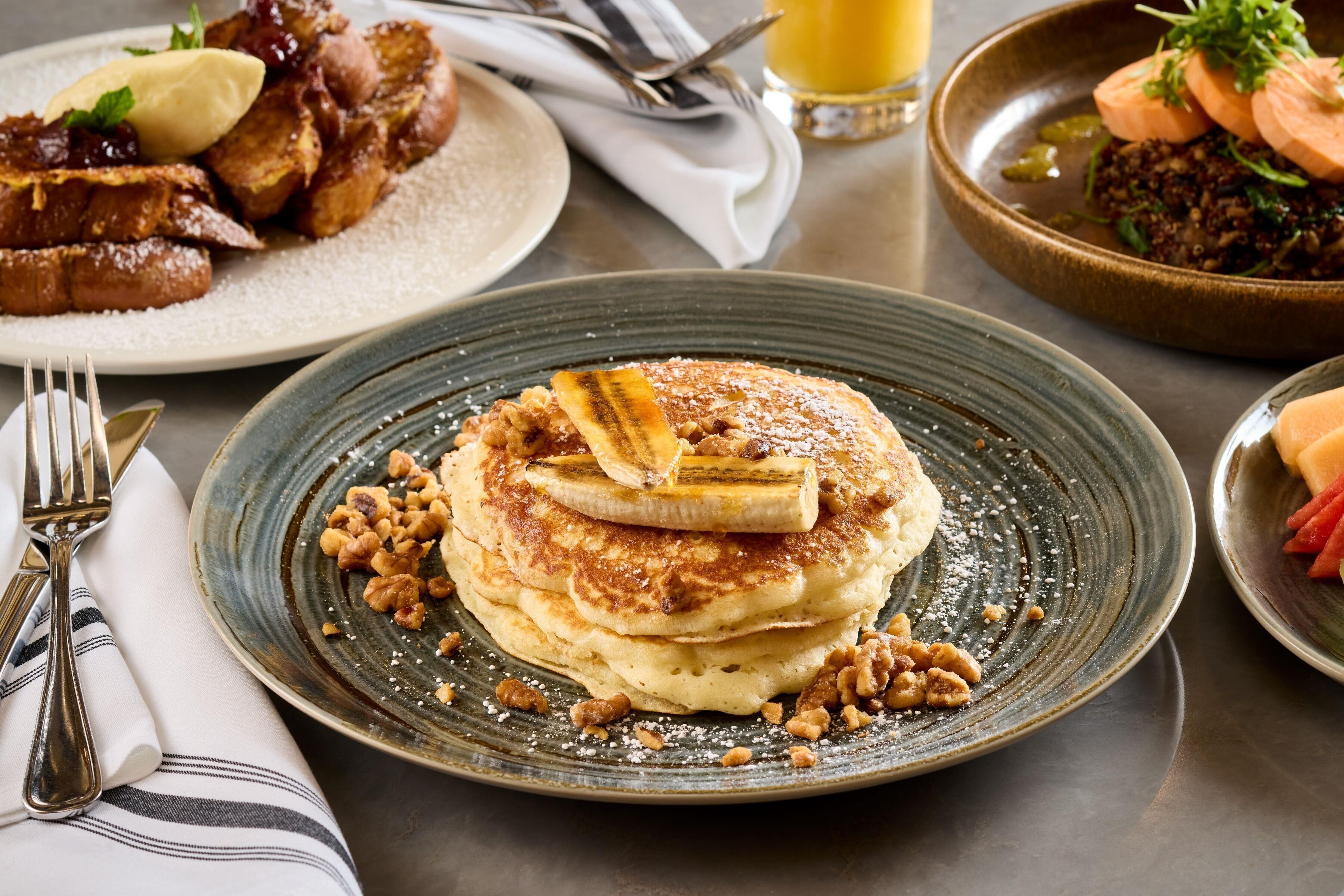 A breakfast setting with pancakes, a plate of French toast, and a bowl of fruit.