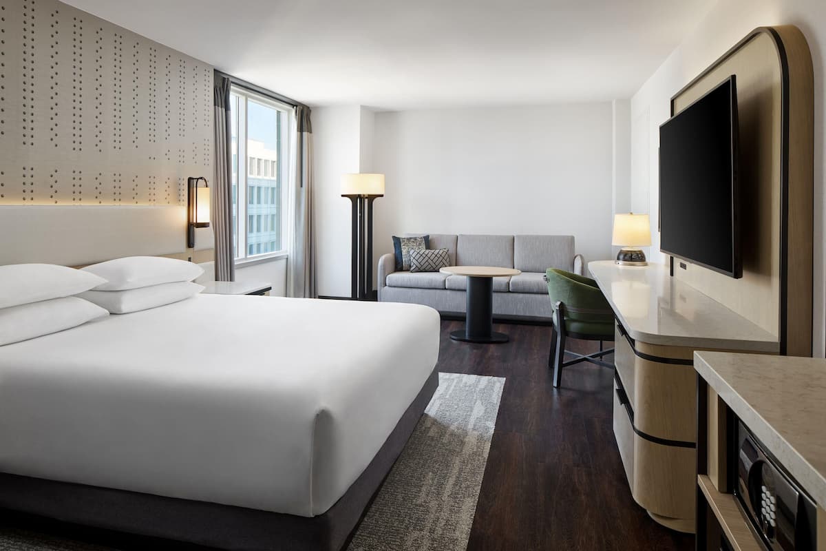 Ein Hotelzimmer mit einem großen Bett, einer Couch, einem Fernseher, einem Schreibtisch und einer Lampe.