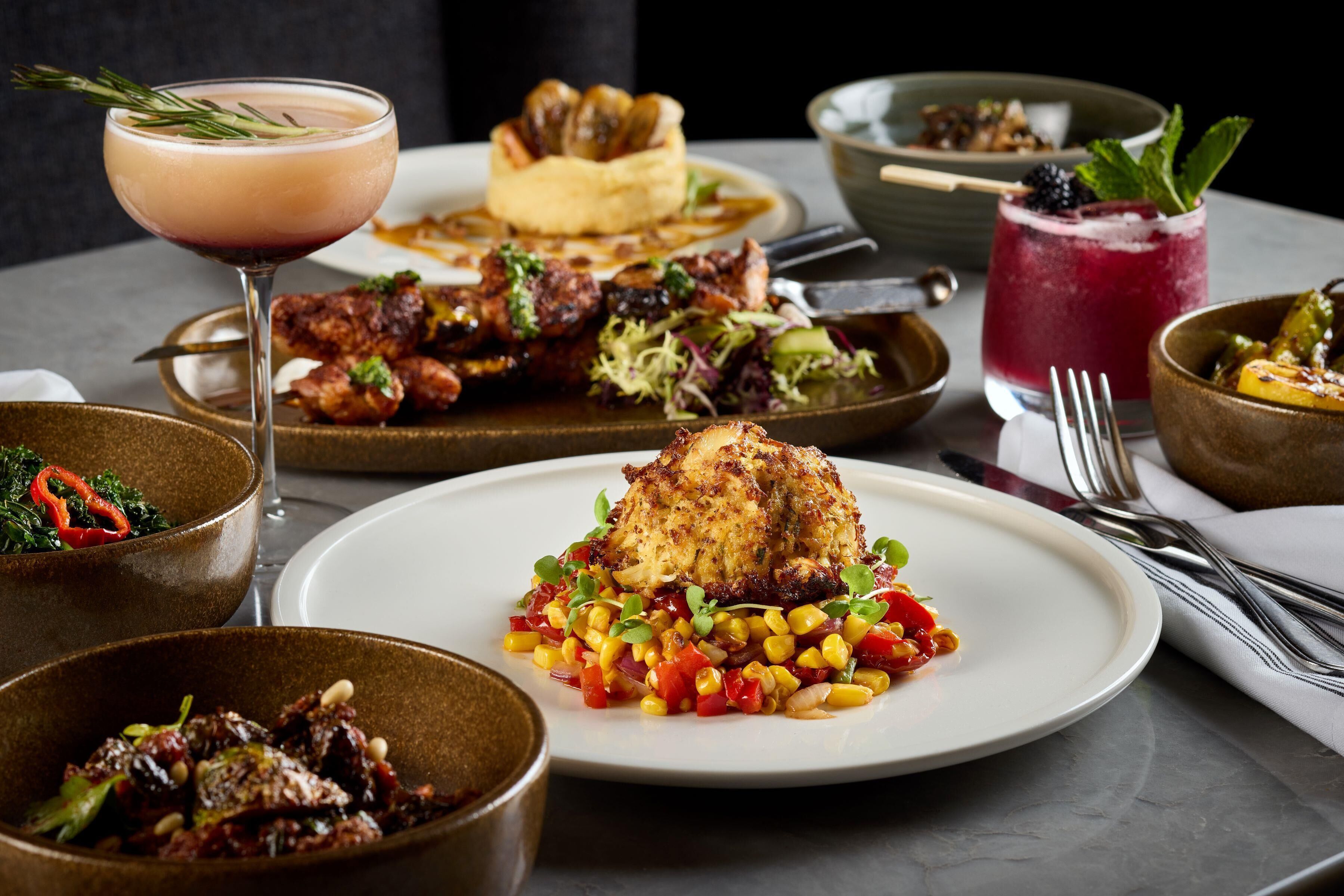 A dining table with various dishes, including a plate of chicken, a bowl of salad, and a glass of drink.