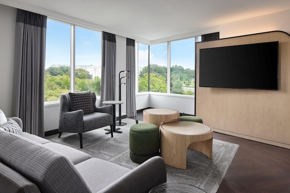 A modern hotel room with a large window, a flat-screen TV, a sofa, a chair, and two ottomans. - Hyatt Regency Washington on Capitol Hill (Washington)