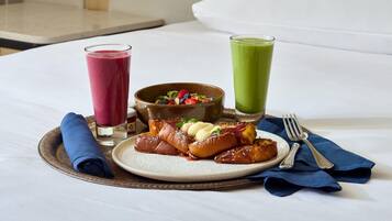 A breakfast tray with pancakes, a bowl of fruit salad, and two glasses of juice on a bed.