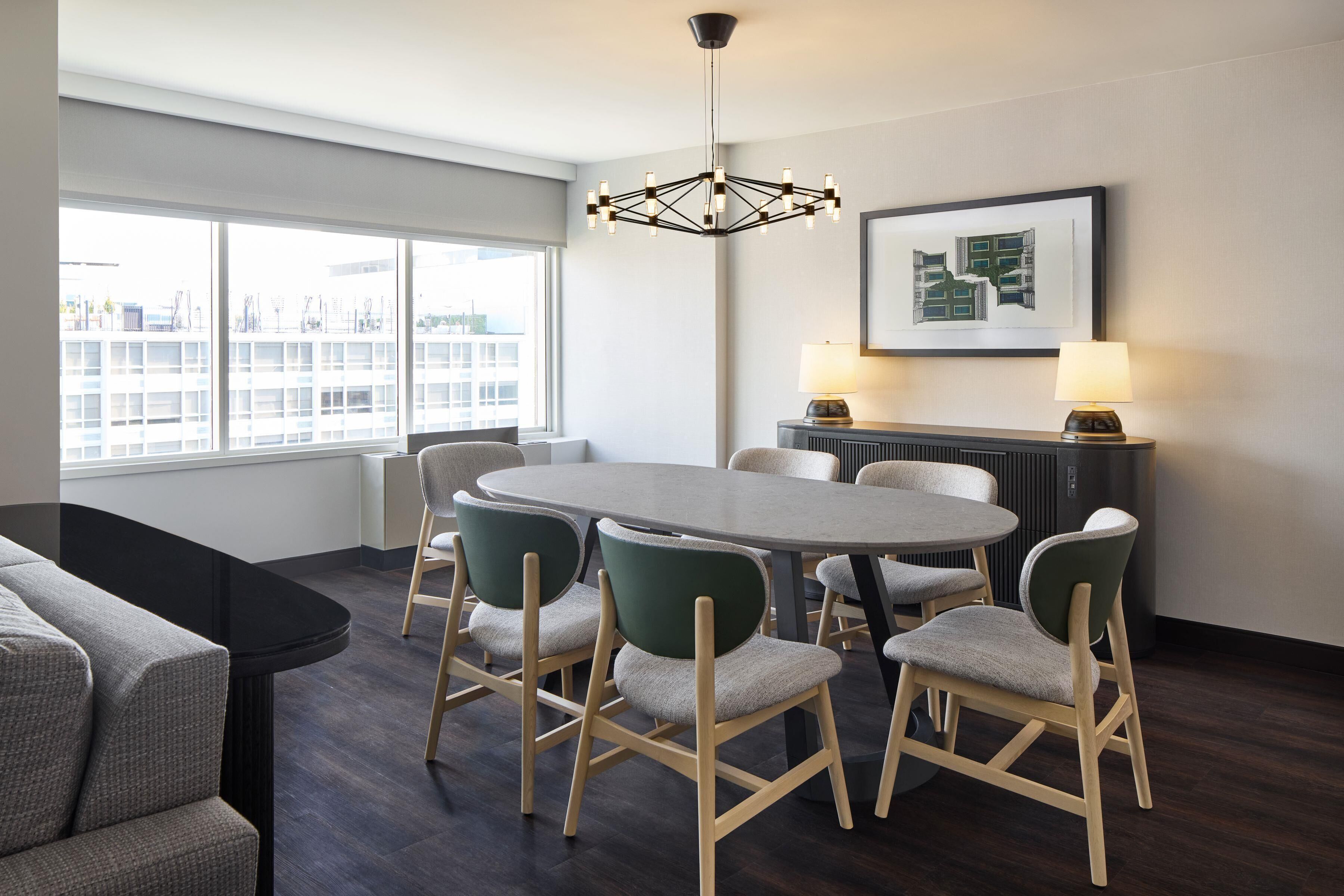 A modern dining area with a round table, six chairs, a chandelier, a radiator, and a framed picture on the wall.