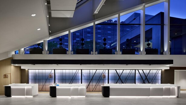 Un moderno hall de hotel con mostrador de recepción, zona de estar y ventanas amplias con vistas a la ciudad.