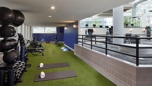 Un gimnasio con equipo de ejercicio, césped artificial verde y un balcón con barandilla.