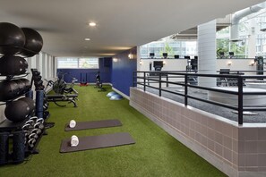 A gym with exercise equipment, green artificial turf, and a balcony with a railing.