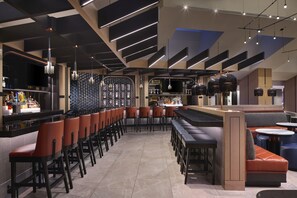 A modern bar area with high stools, a counter with bottles, and a seating area with a sofa and tables. - Hyatt Regency Washington on Capitol Hill (Washington)
