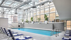 A swimming pool with lounge chairs, potted plants, and a view of buildings through large windows. - Hyatt Regency Washington on Capitol Hill (Washington)